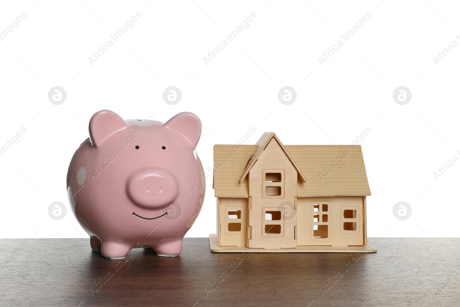 Photo of Piggy bank and house model on wooden table against white background. Saving money concept