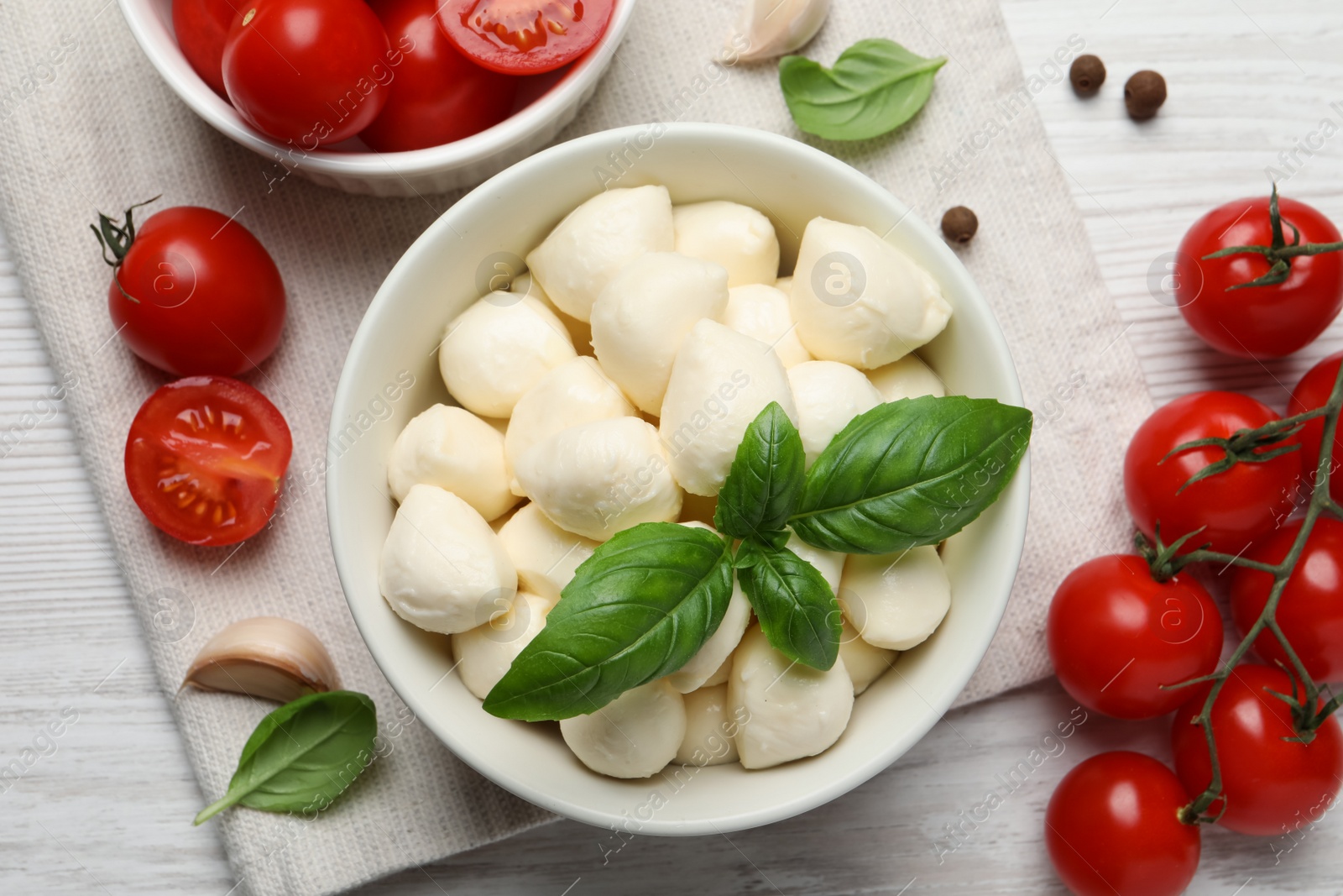 Photo of Delicious mozzarella balls in bowl, tomatoes and basil leaves on white wooden table, flat lay