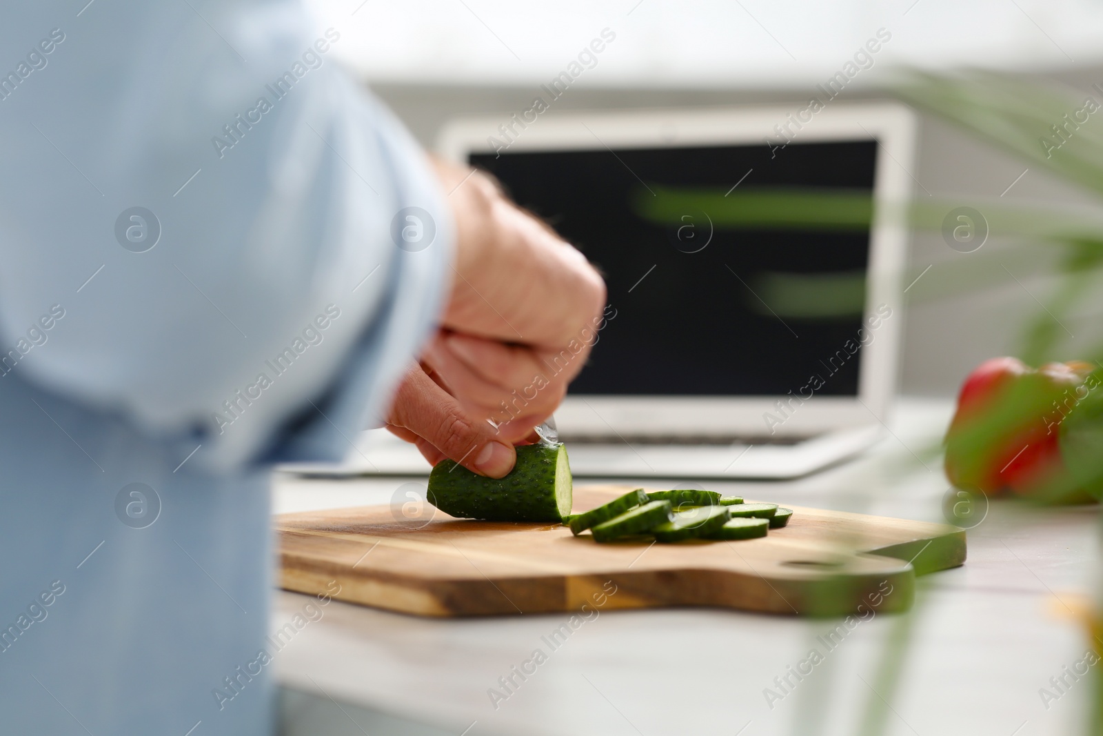 Photo of Man making dinner while watching online cooking course via laptop in kitchen, closeup