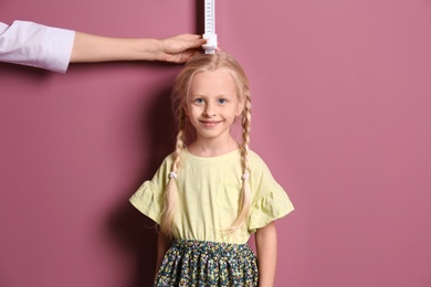Photo of Doctor measuring little girl's height on color background