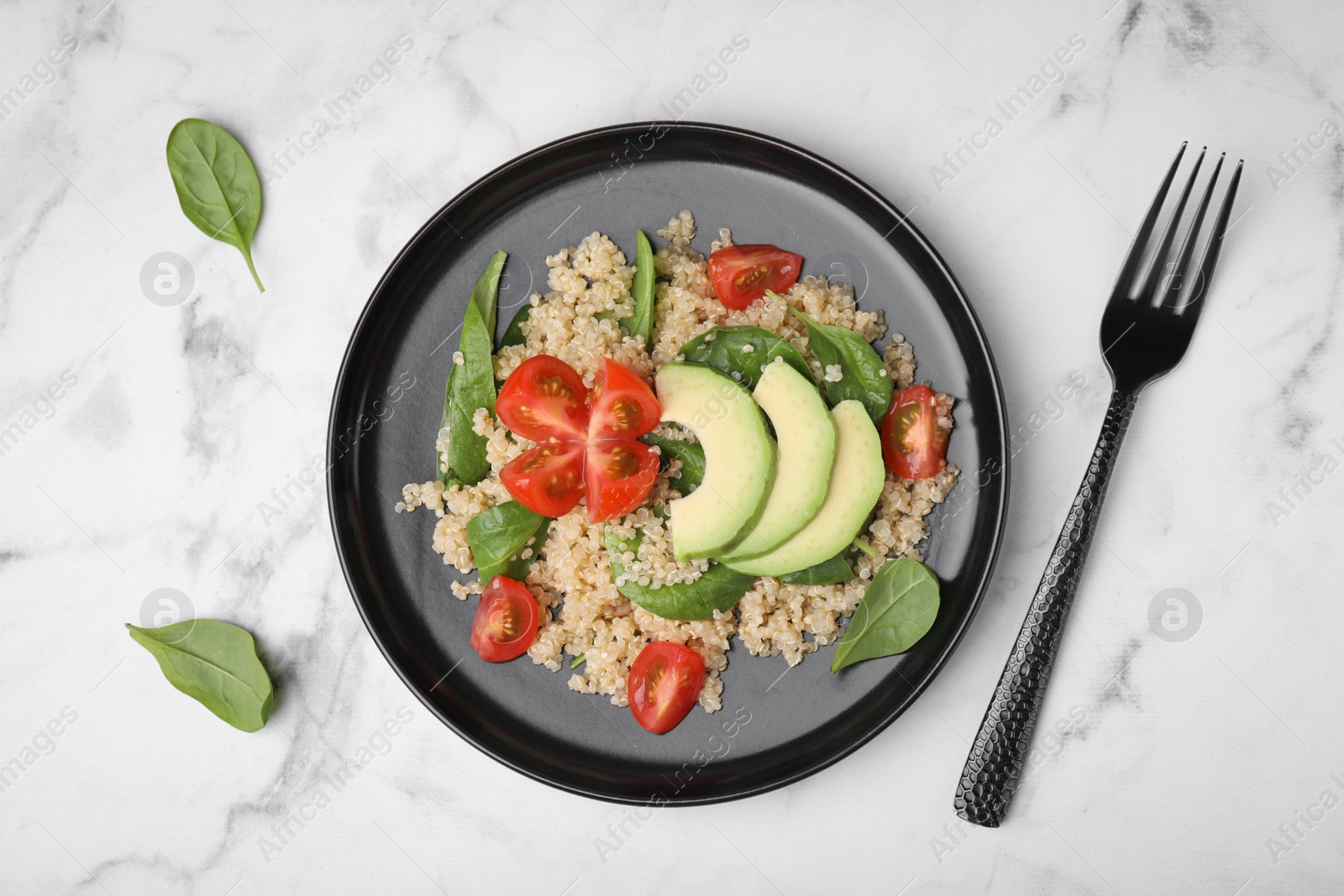 Photo of Delicious quinoa salad with tomatoes, avocado slices and spinach leaves served on white marble table, flat lay