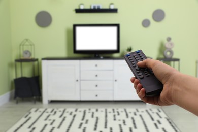 Photo of Young man switching channels on TV set with remote control at home, closeup