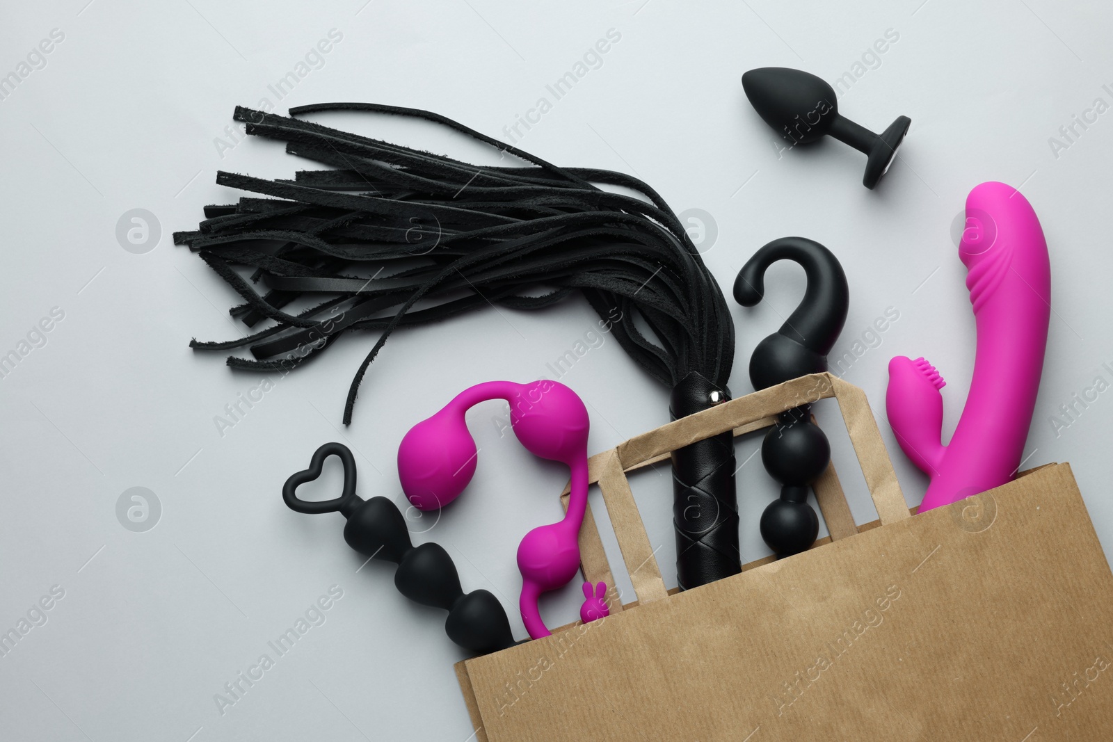 Photo of Paper shopping bag with different sex toys on white background, flat lay