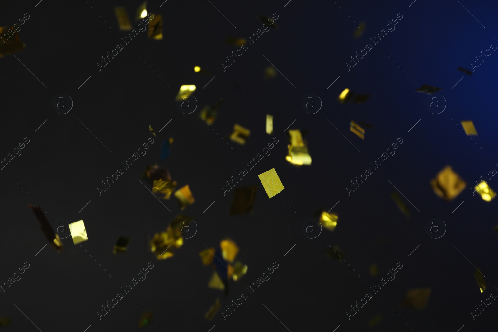 Photo of Shiny golden confetti falling down on dark blue background