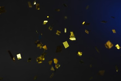 Shiny golden confetti falling down on dark blue background