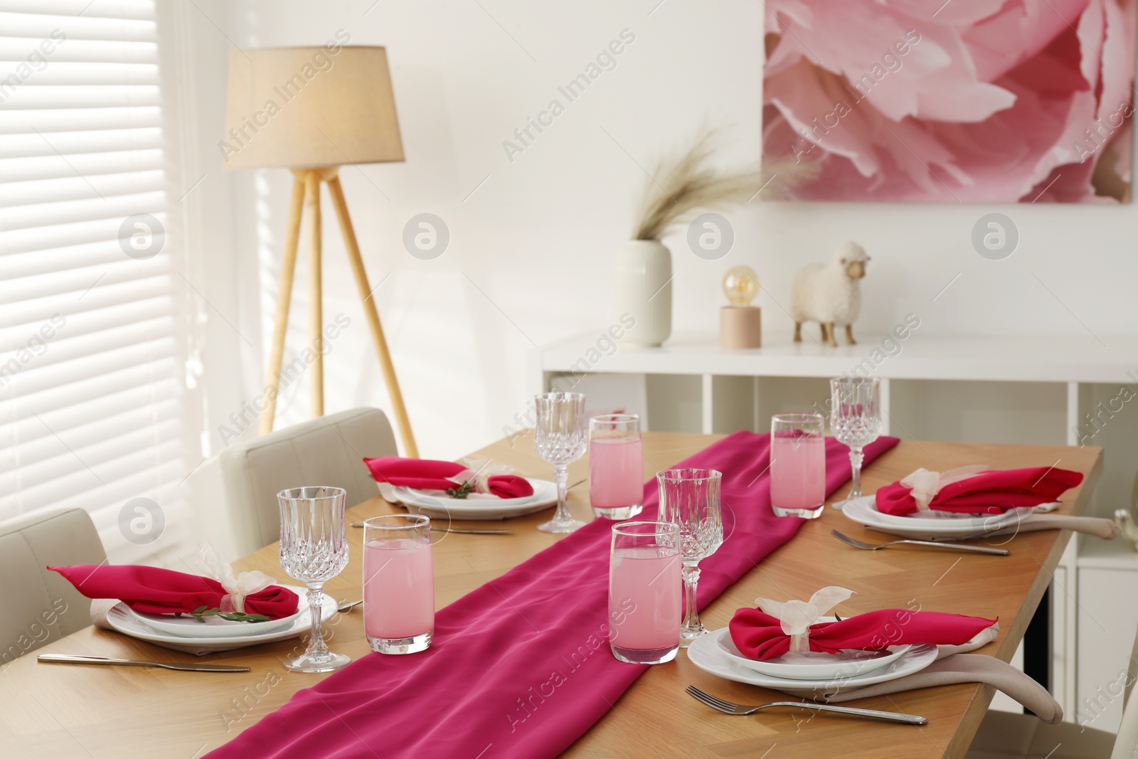 Photo of Color accent table setting. Glasses, plates and pink napkins in dining room