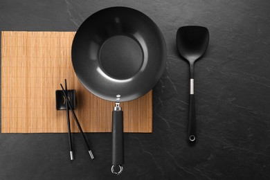 Black metal wok, chopsticks and spatula on dark textured table, top view