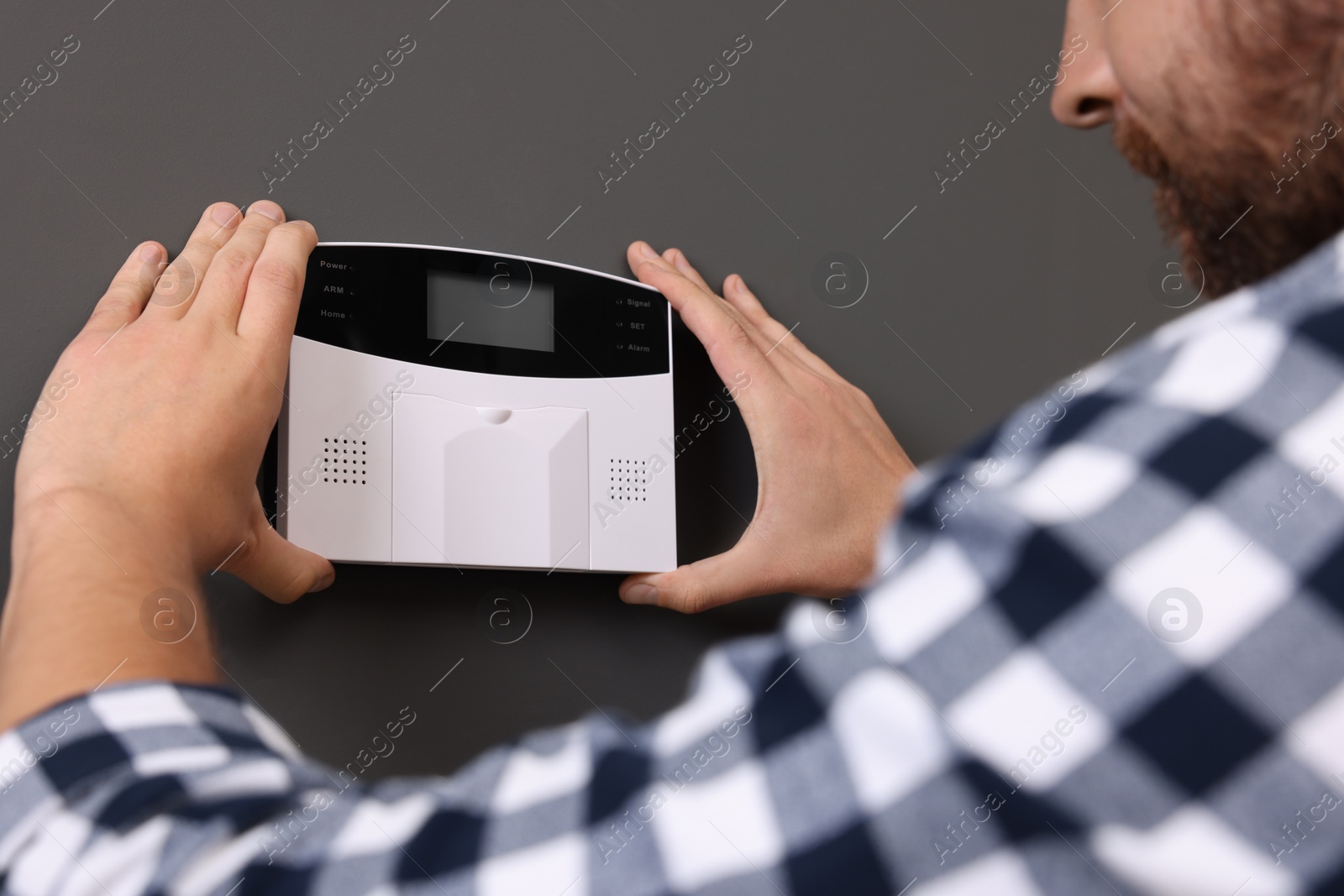 Photo of Man installing home security alarm system on gray wall, closeup