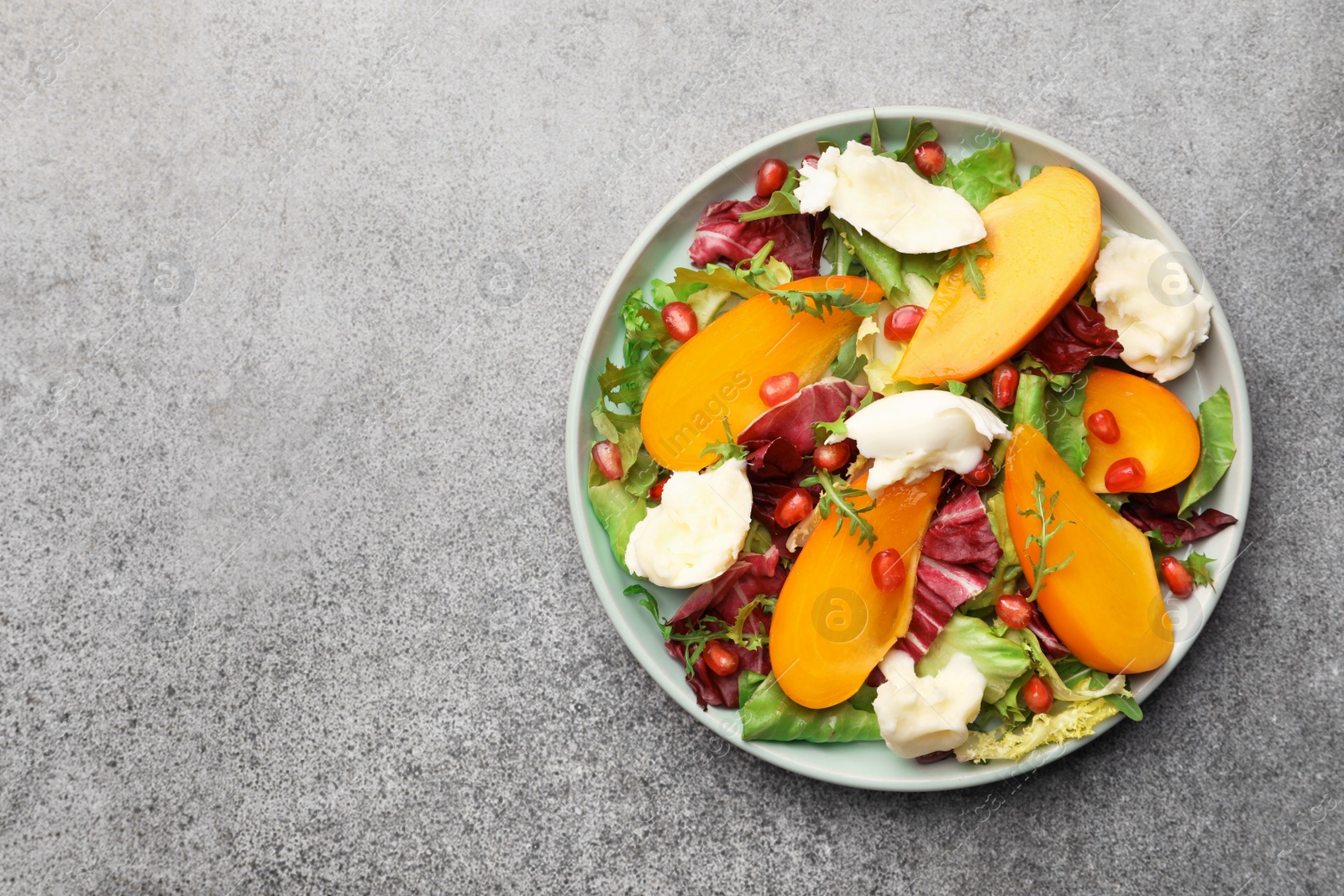 Photo of Delicious persimmon salad with cheese and pomegranate on grey table, top view. Space for text