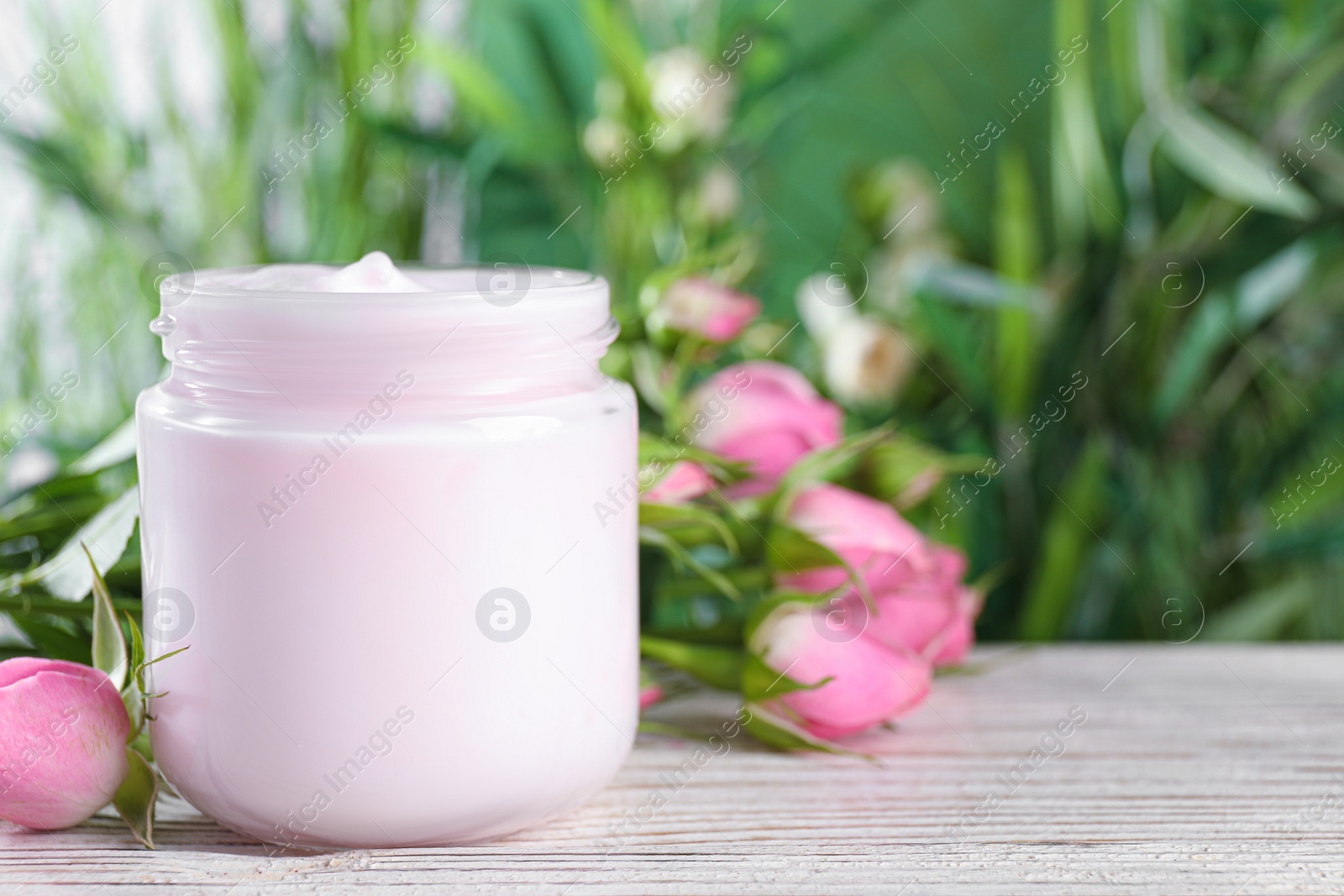 Photo of Jar of hand cream and roses on white wooden table, space for text