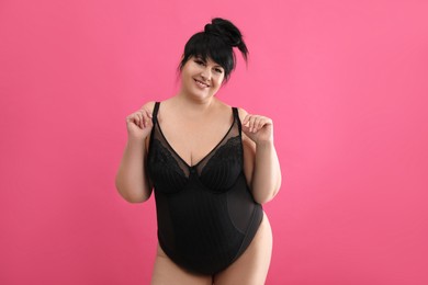 Beautiful overweight woman in black underwear on pink background. Plus-size model