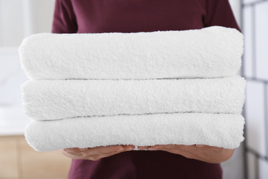 Photo of Woman holding fresh towels in bathroom, closeup