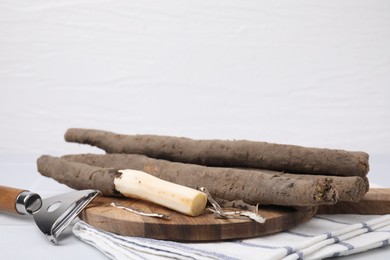Photo of Raw salsify roots and peeler on white table