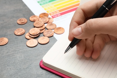 Photo of Woman with pen, notebook, coins and energy efficiency rating chart at table, closeup