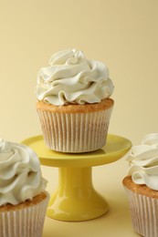 Photo of Tasty vanilla cupcakes with cream on pale yellow background, closeup