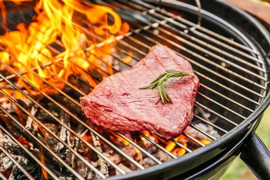 Photo of Tasty meat on barbecue grill with fire flames outdoors, closeup