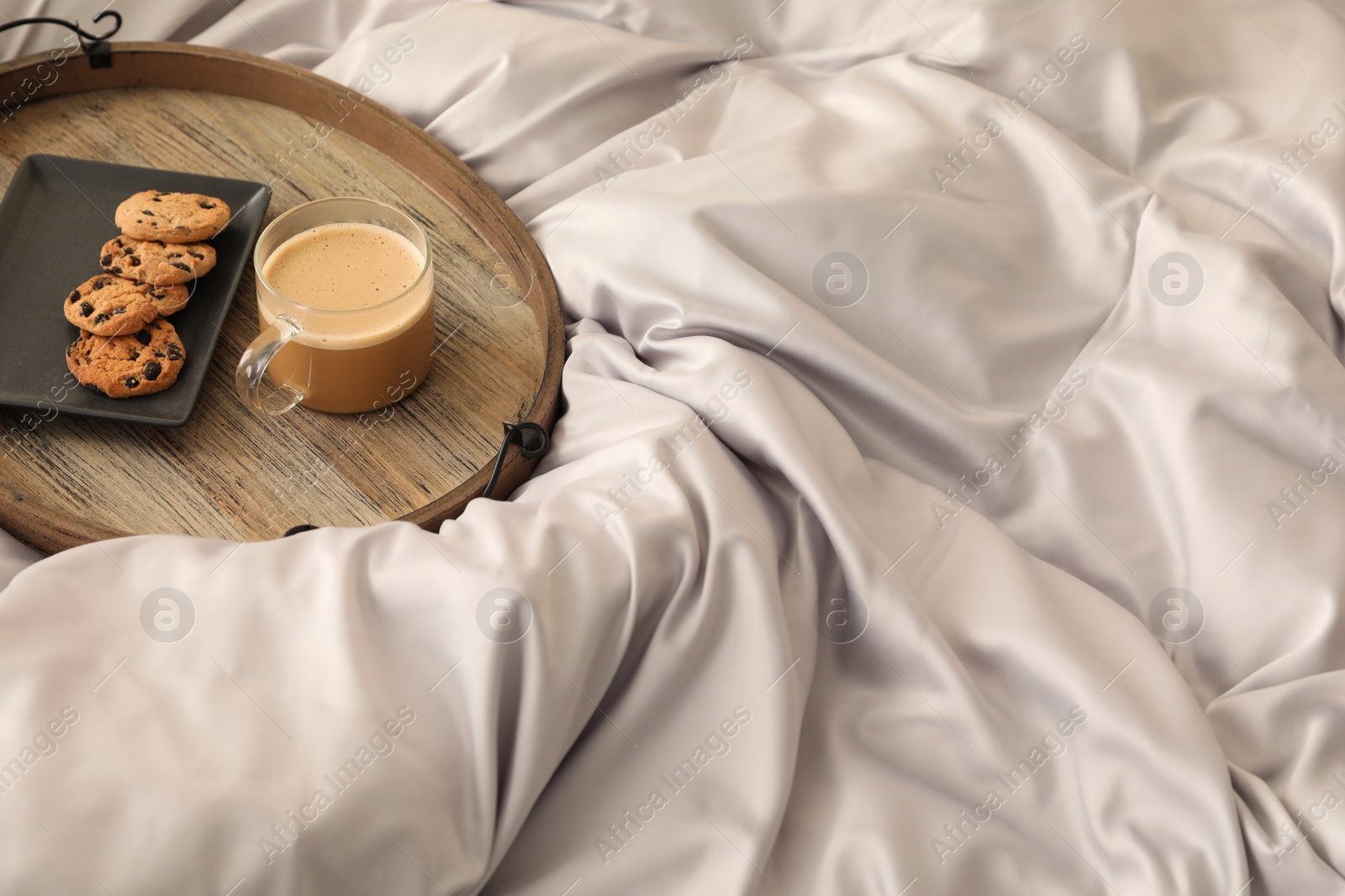 Photo of Delicious cookies and cup of coffee on bed with stylish silky linens, space for text