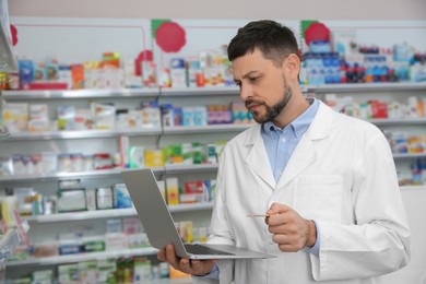 Photo of Concentrated pharmacist with laptop in modern drugstore