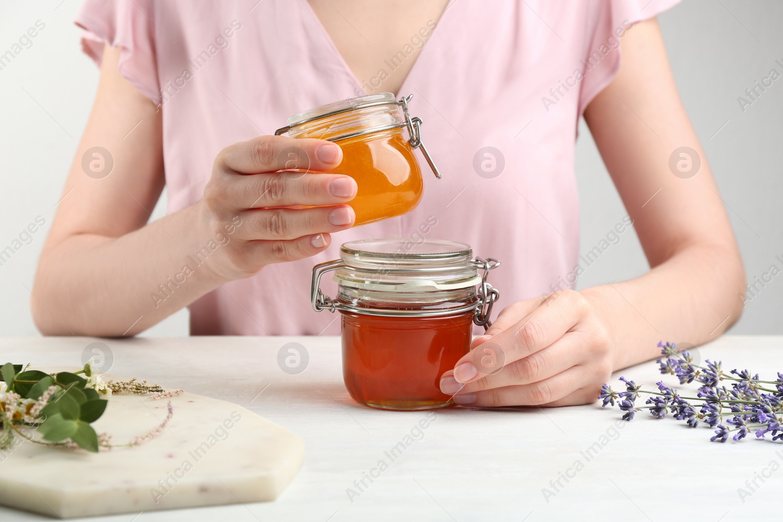 Photo of Woman holding jars with different types of honey at white table, closeup