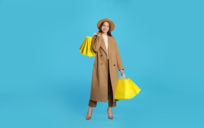 Photo of Happy young woman with shopping bags on light blue background. Big sale