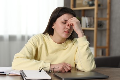 Overwhelmed woman sitting with laptop at table indoors