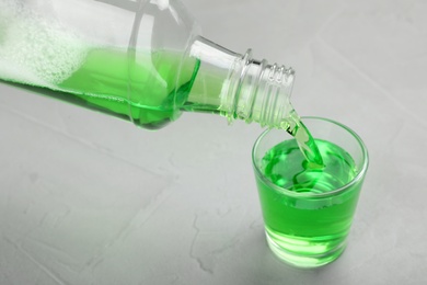 Pouring mouthwash in glass on light background. Teeth care