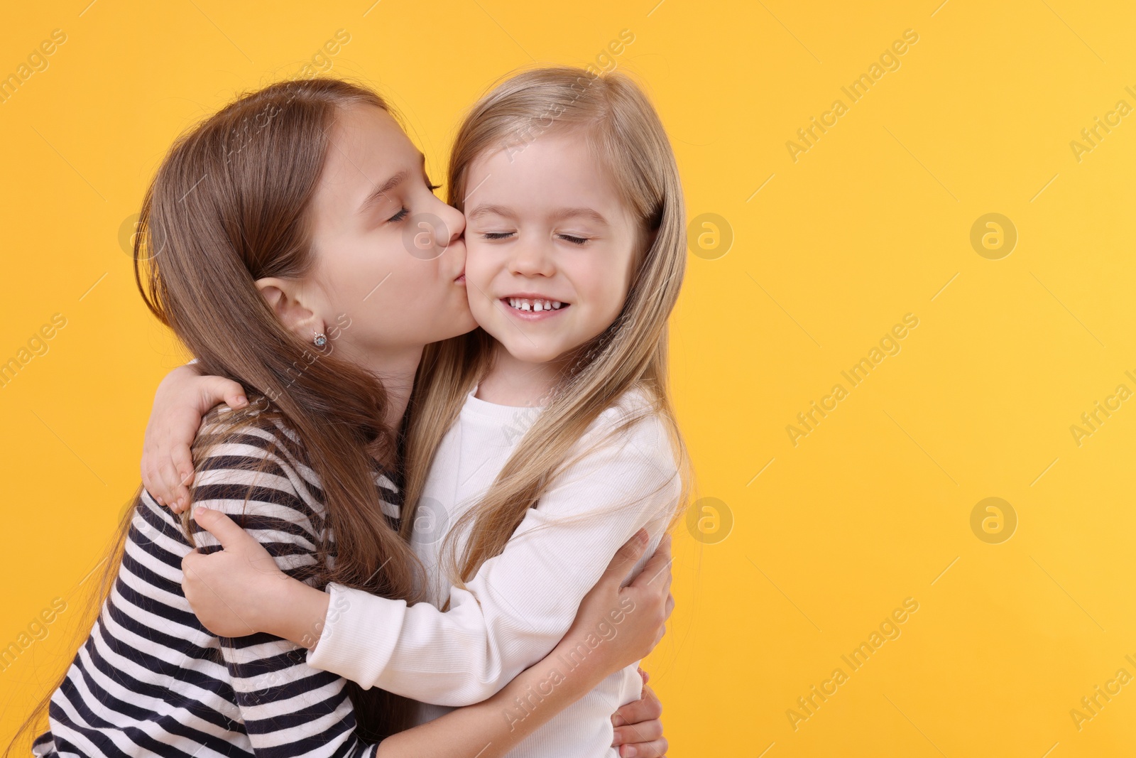 Photo of Portrait of cute little sisters on orange background, space for text