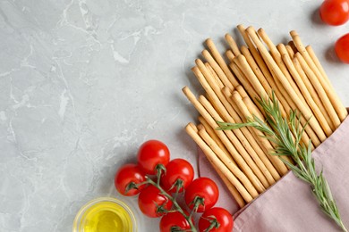 Photo of Delicious grissini sticks, oil, rosemary and tomatoes on grey marble table, flat lay. Space for text