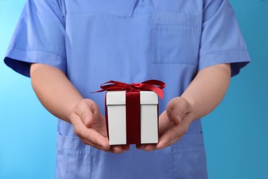 Photo of Doctor holding gift box on light blue background, closeup. Medical present