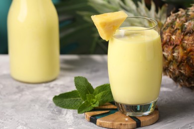 Photo of Tasty pineapple smoothie, mint and fruit on grey textured table. Space for text