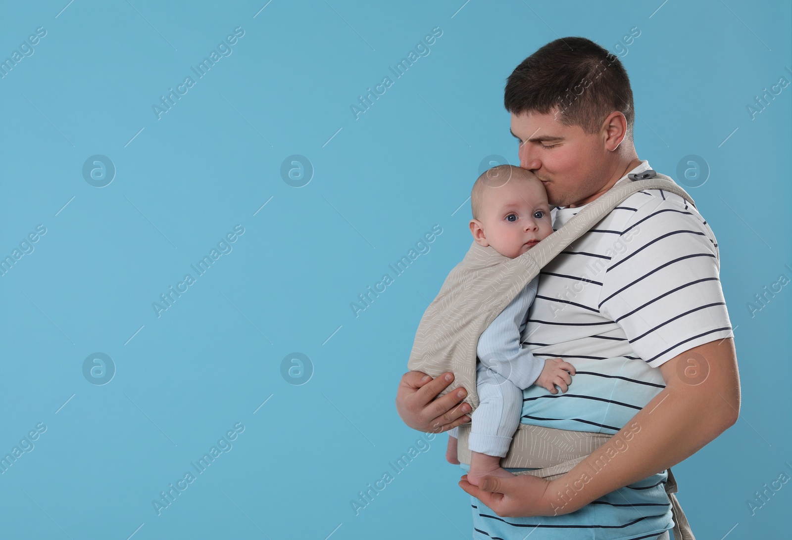 Photo of Father holding his child in sling (baby carrier) on light blue background. Space for text