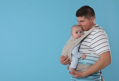 Father holding his child in sling (baby carrier) on light blue background. Space for text