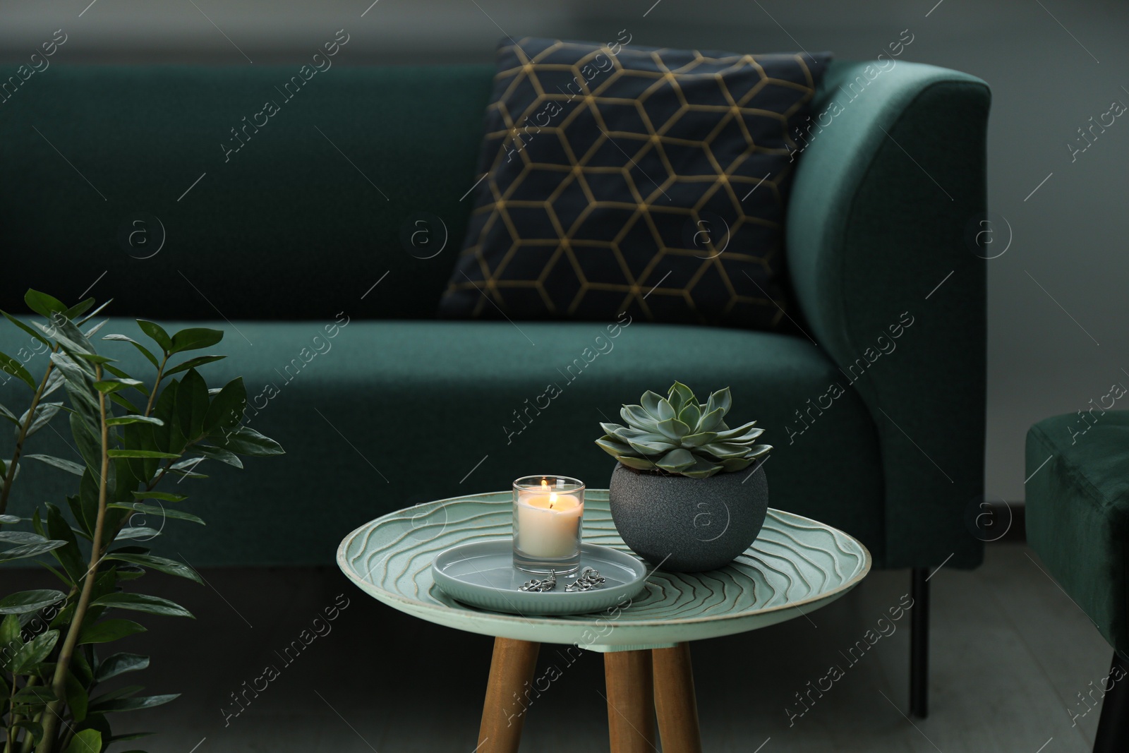 Photo of Burning candle and houseplant on side table near sofa in living room