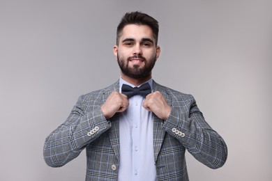 Photo of Portrait of smiling man adjusting bow tie on grey background