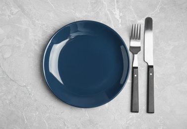 Photo of Empty blue ceramic plate and cutlery on light grey marble table, flat lay