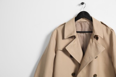 Photo of Hanger with beige trench coat on white wall, space for text