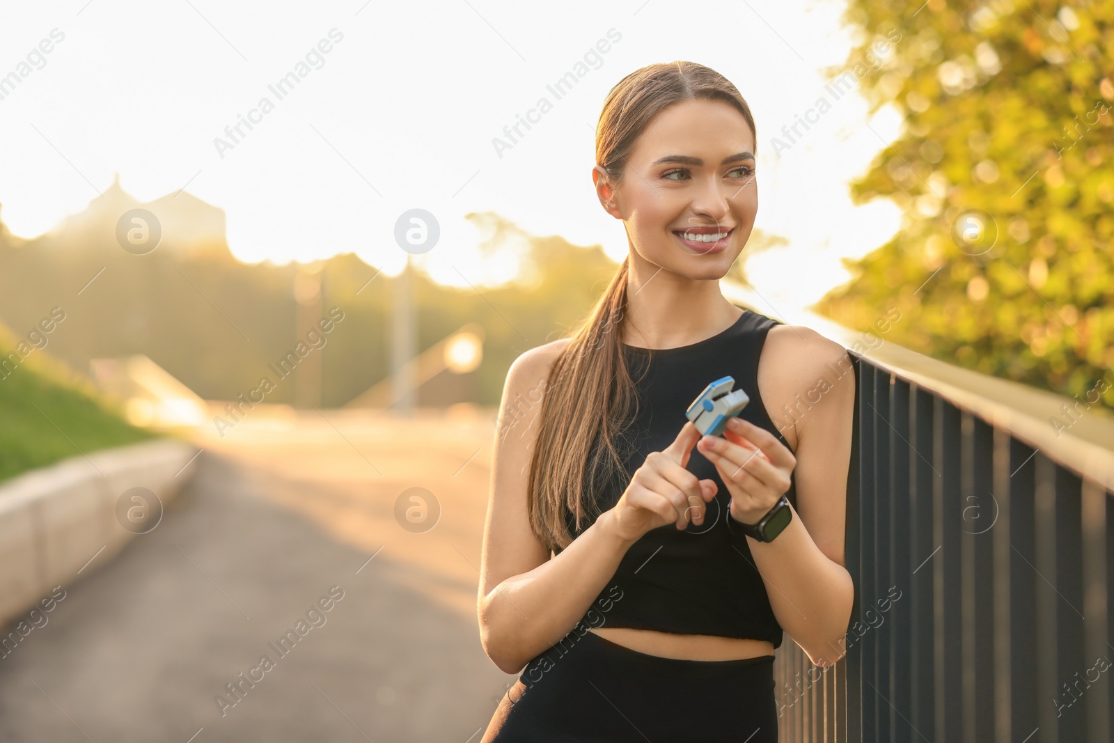 Photo of Happy woman checking pulse with blood pressure monitor on finger after training outdoors. Space for text