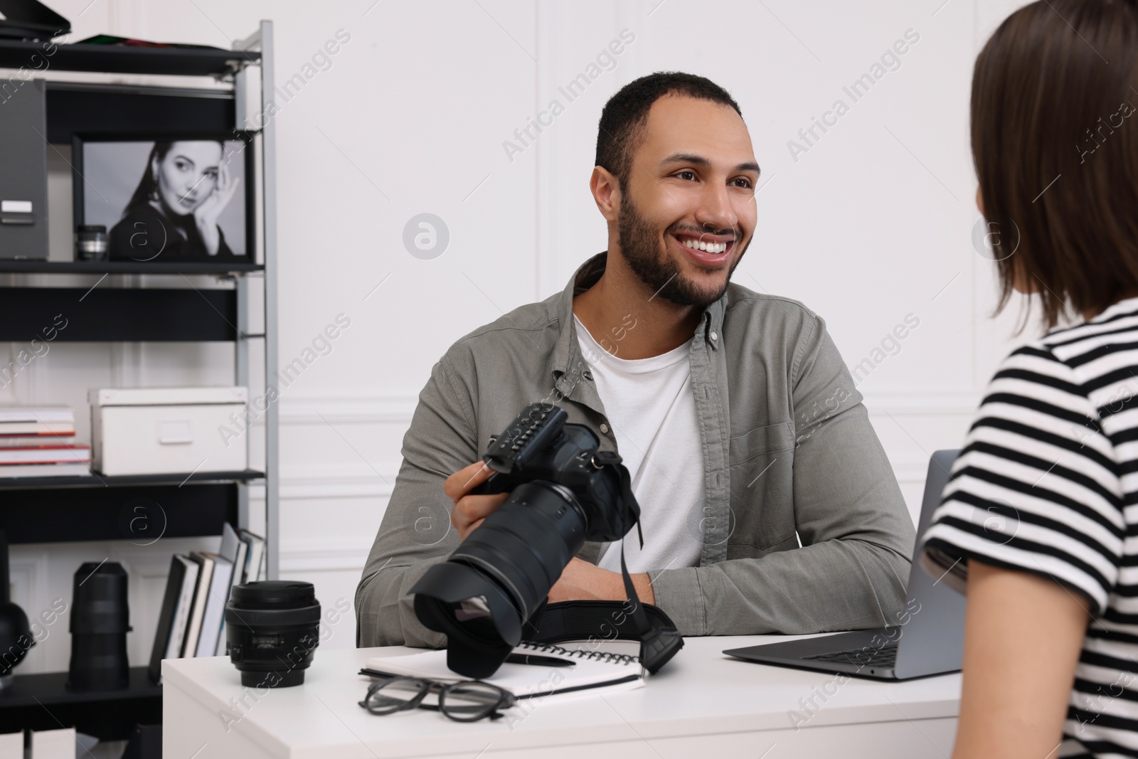 Photo of Young professional photographer holding camera while talking with woman in modern photo studio