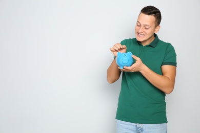 Young man putting coin into piggy bank on white background. Space for text