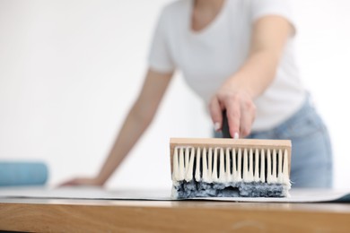 Photo of Woman applying glue onto wallpaper sheet at table indoors, closeup