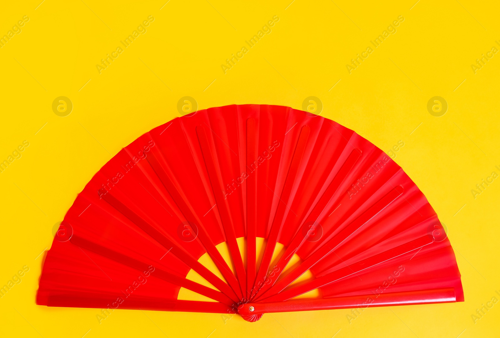 Photo of Red hand fan on yellow background, top view