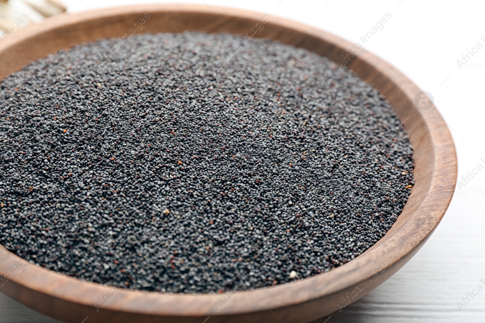 Photo of Poppy seeds in wooden bowl on white table, closeup
