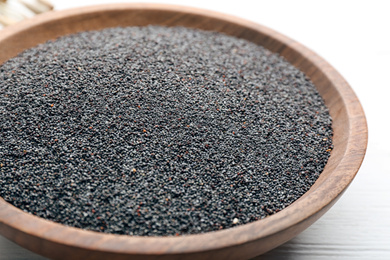 Poppy seeds in wooden bowl on white table, closeup