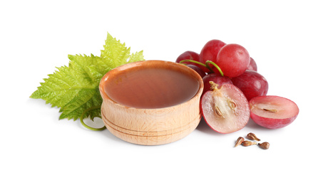 Photo of Organic red grapes, seeds and bowl of natural essential oil on white background