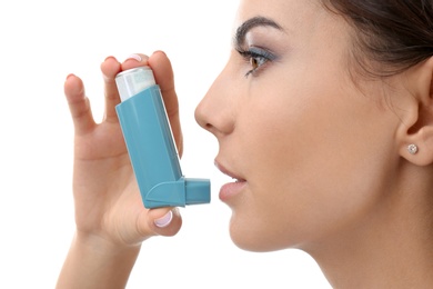 Young woman using asthma inhaler on white background, closeup