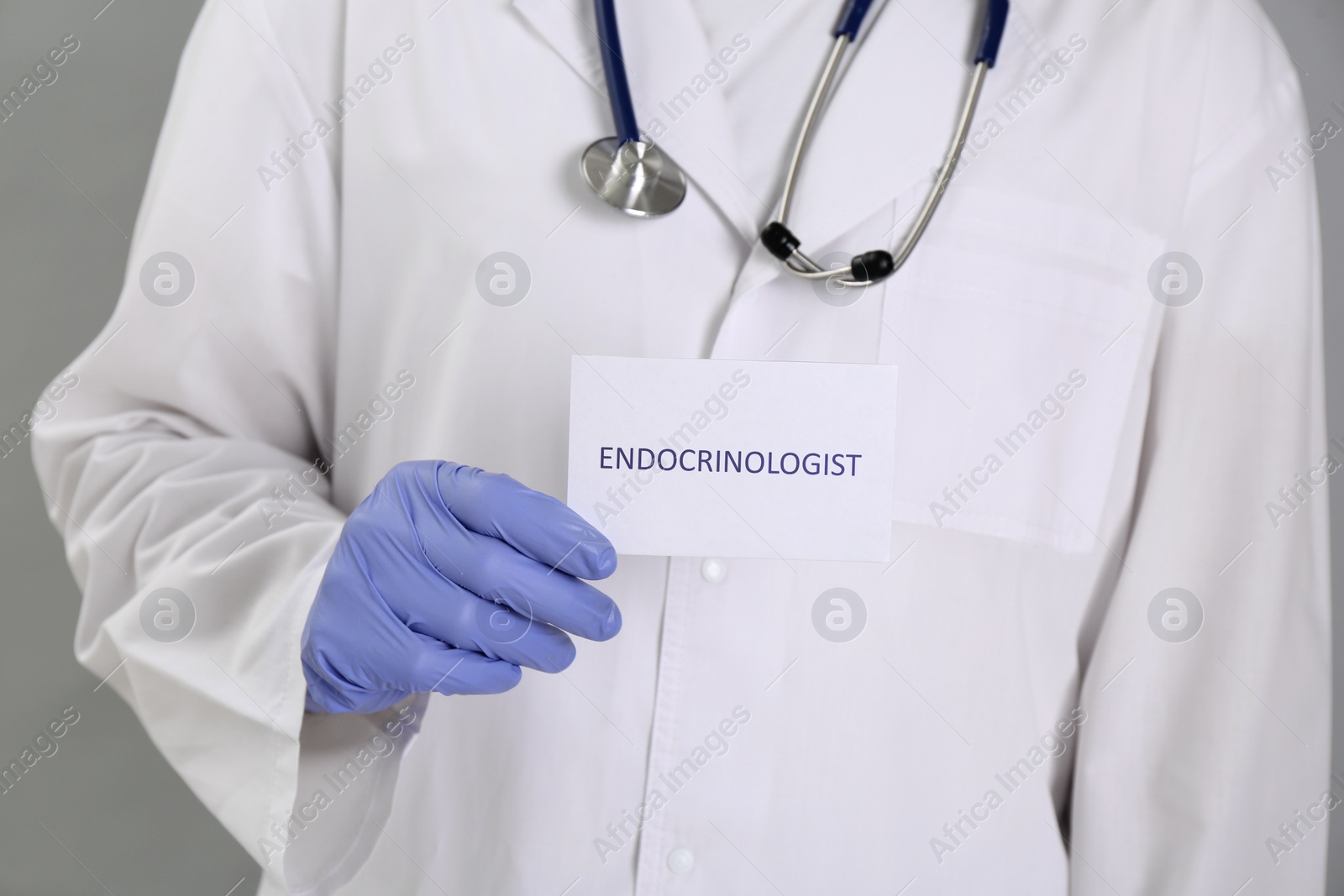 Image of Endocrinologist with stethoscope holding card on grey background, closeup