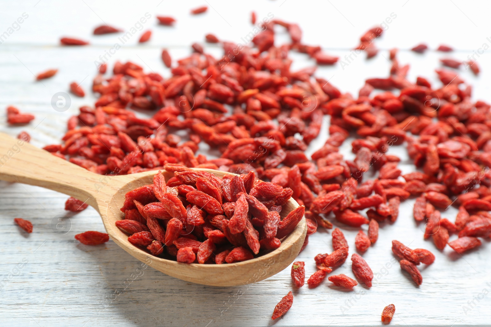 Photo of Spoon and dried goji berries on white wooden table, closeup. Healthy superfood