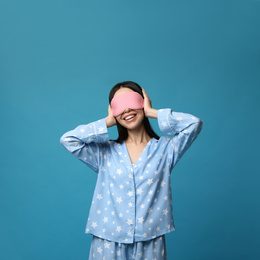 Photo of Young woman wearing pajamas and sleeping mask on blue background. Bedtime