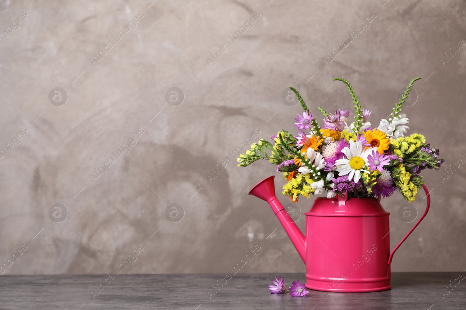 Photo of Watering can with beautiful wild flowers on table against grey background