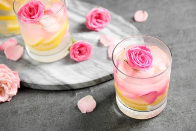 Delicious refreshing drink with lemon and roses on grey table